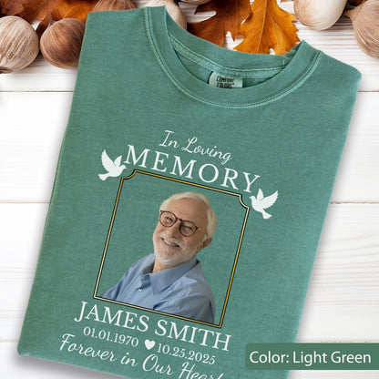 May include: A light green t-shirt featuring a memorial graphic with the text In Loving Memory, a photograph of a smiling person with glasses, the name James Smith, the dates 01.01.1970 and 10.25.2025, and two white dove illustrations.