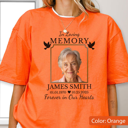 May include: An orange t-shirt featuring a memorial graphic with the text In Loving Memory, the name James Smith, the dates 01.01.1970 and 10.25.2025, and the phrase Forever in Our Hearts, centered around a photograph of an older person with gray hair.