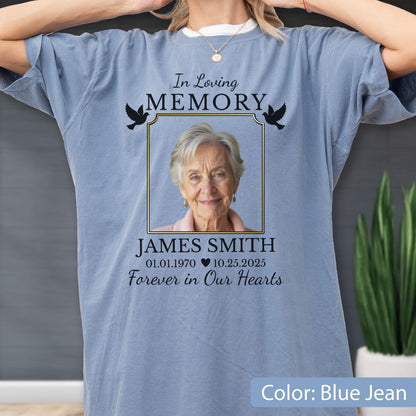 May include: A blue jean colored t-shirt featuring a memorial graphic with a photograph of an older person, the text In Loving Memory, the name JAMES SMITH, the dates 01.01.1970 and 10.25.2025, a heart icon, the phrase Forever in Our Hearts, and two black birds.