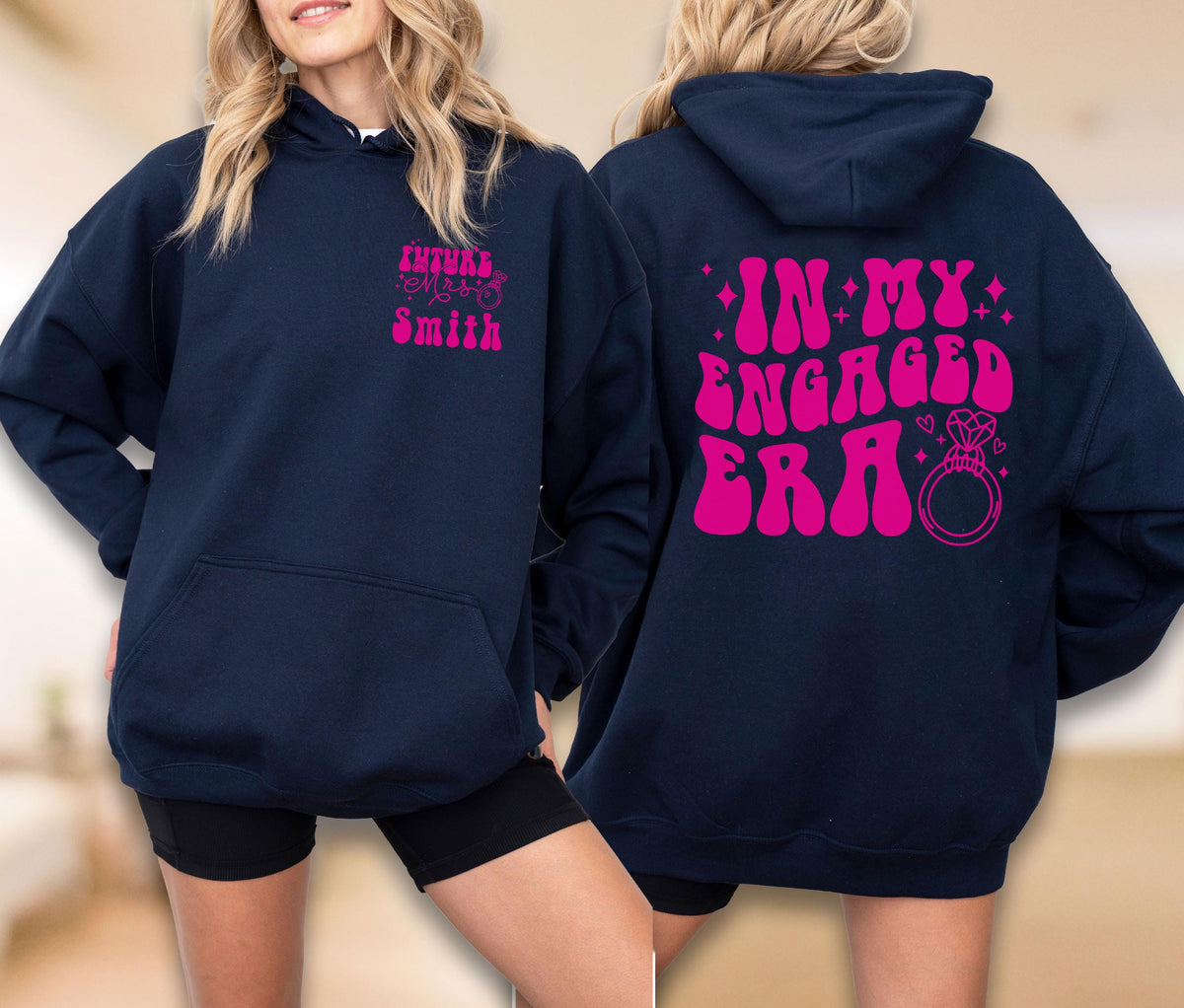 May include: A navy blue hooded sweatshirt featuring bright pink text. The front displays "FUTURE MRS. SMITH" on the left chest. The back features the text "IN MY ENGAGED ERA" in a bold, wavy font, accompanied by a graphic of a diamond engagement ring.