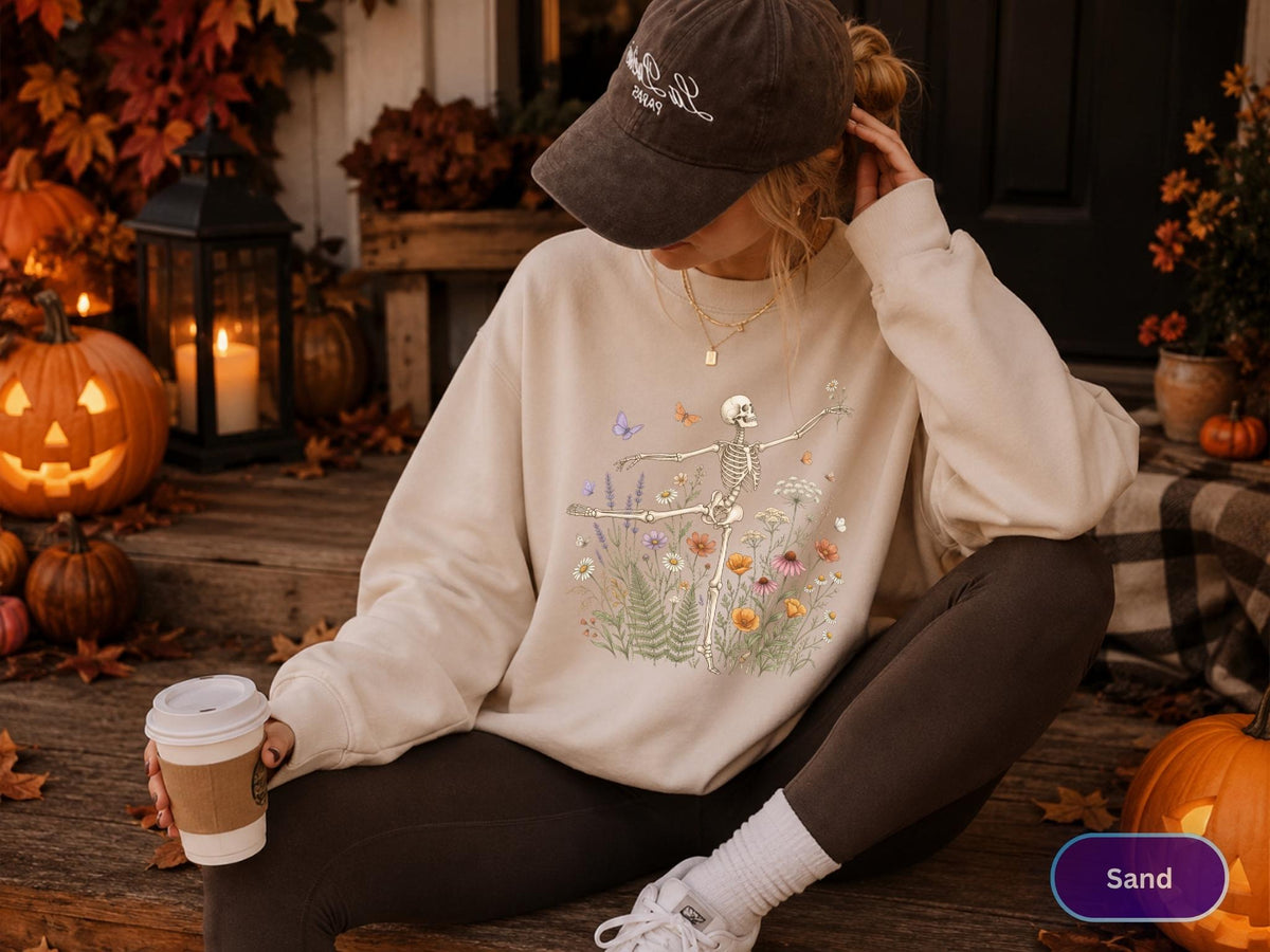 May include: A beige crewneck sweatshirt featuring a graphic print of a skeleton dancing amidst a colorful arrangement of wildflowers, ferns, and butterflies. The long-sleeved pullover has a ribbed collar, cuffs, and hem, providing a relaxed fit.