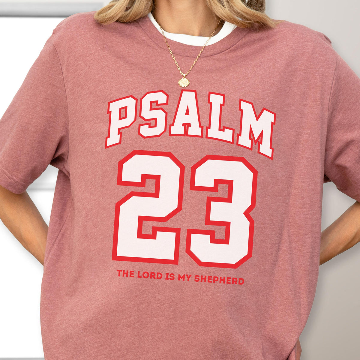 May include: A mauve short-sleeve t-shirt featuring the white text PSALM 23 in a collegiate font, with the number 23 in large white block lettering outlined in red, and the text THE LORD IS MY SHEPHERD printed in red below the number.