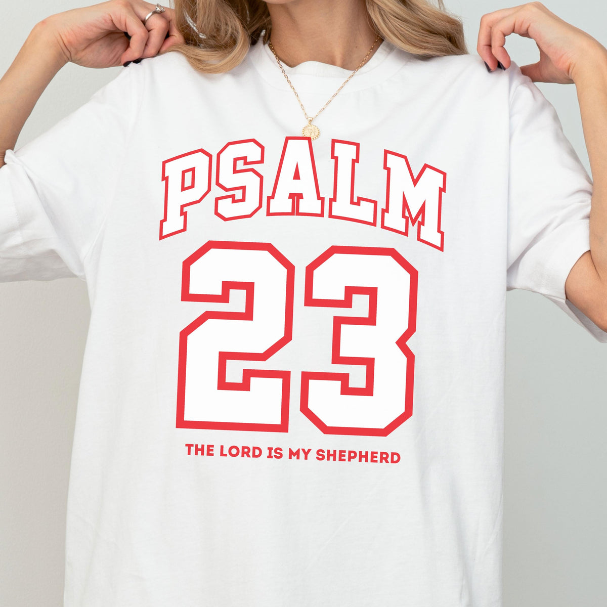 May include: A white short-sleeved t-shirt featuring red collegiate-style lettering that reads PSALM 23. Below the large number 23, the text THE LORD IS MY SHEPHERD is printed in a smaller red sans-serif font. The shirt has a crew neckline.