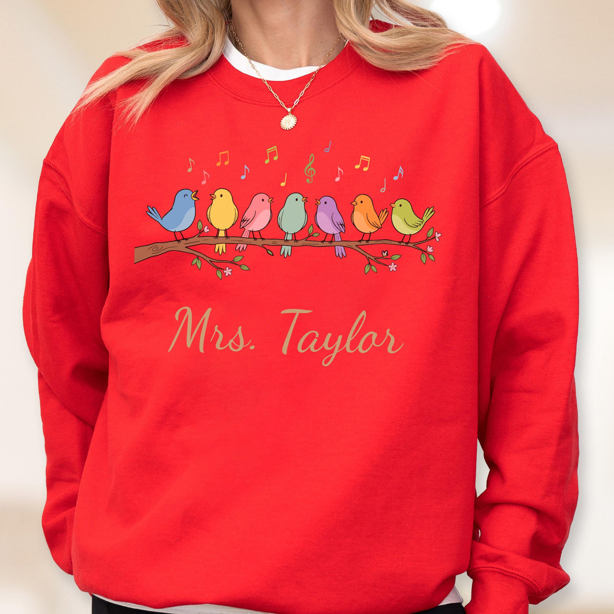 May include: A bright red crewneck sweatshirt featuring a graphic of seven colorful birds perched on a brown tree branch. Above the birds are small musical notes in various colors. The text "Mrs. Taylor" is printed in a gold script font below.