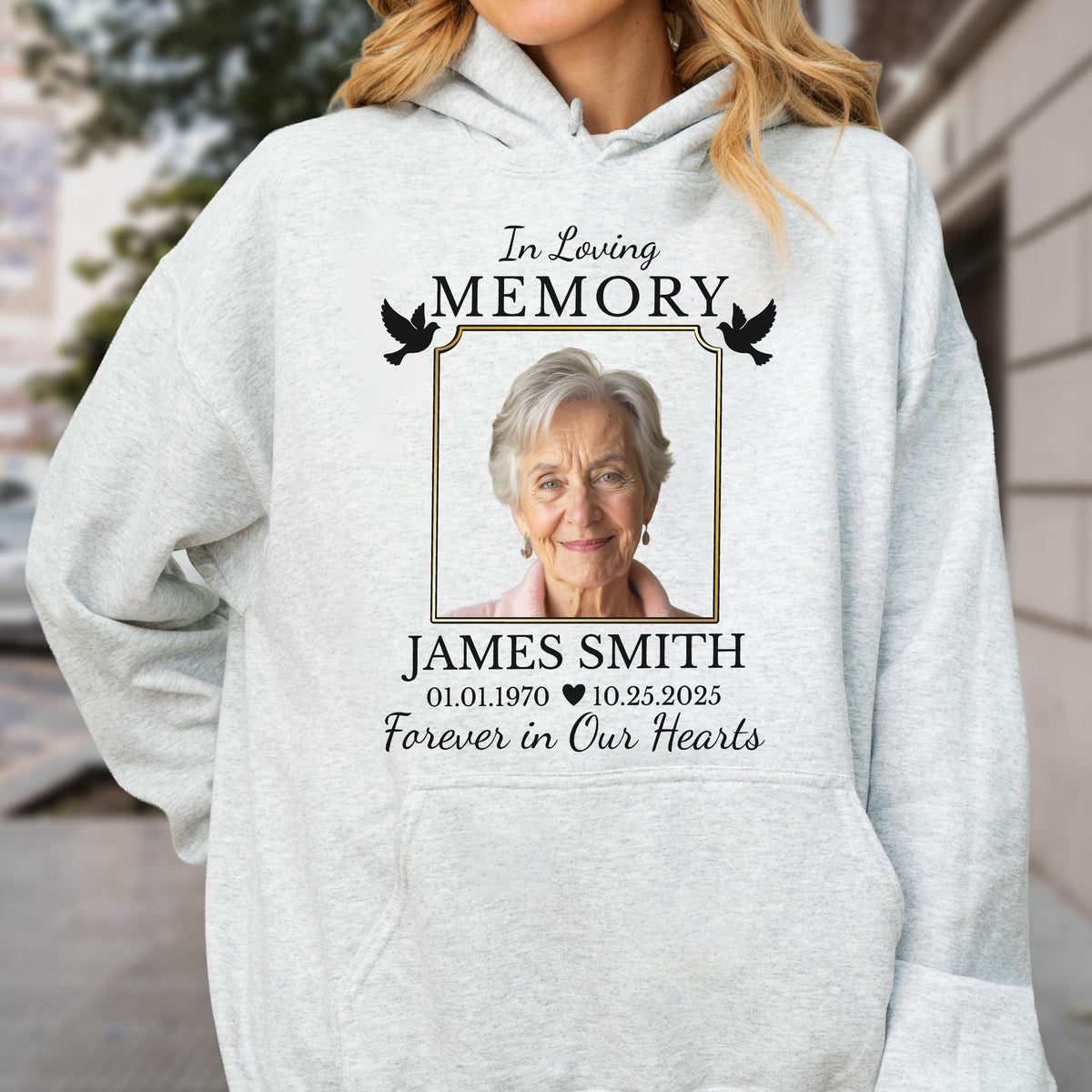 May include: A light gray hooded sweatshirt featuring a memorial graphic with a photograph of an older person. The text reads In Loving Memory, James Smith, 01.01.1970, 10.25.2025, and Forever in Our Hearts, accompanied by two black bird silhouettes.