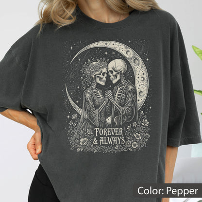 May include: A pepper-colored t-shirt featuring a graphic of two skeletons holding hands under a crescent moon. The skeletons are surrounded by flowers and stars. The text "FOREVER & ALWAYS" is printed in a serif font below the figures.