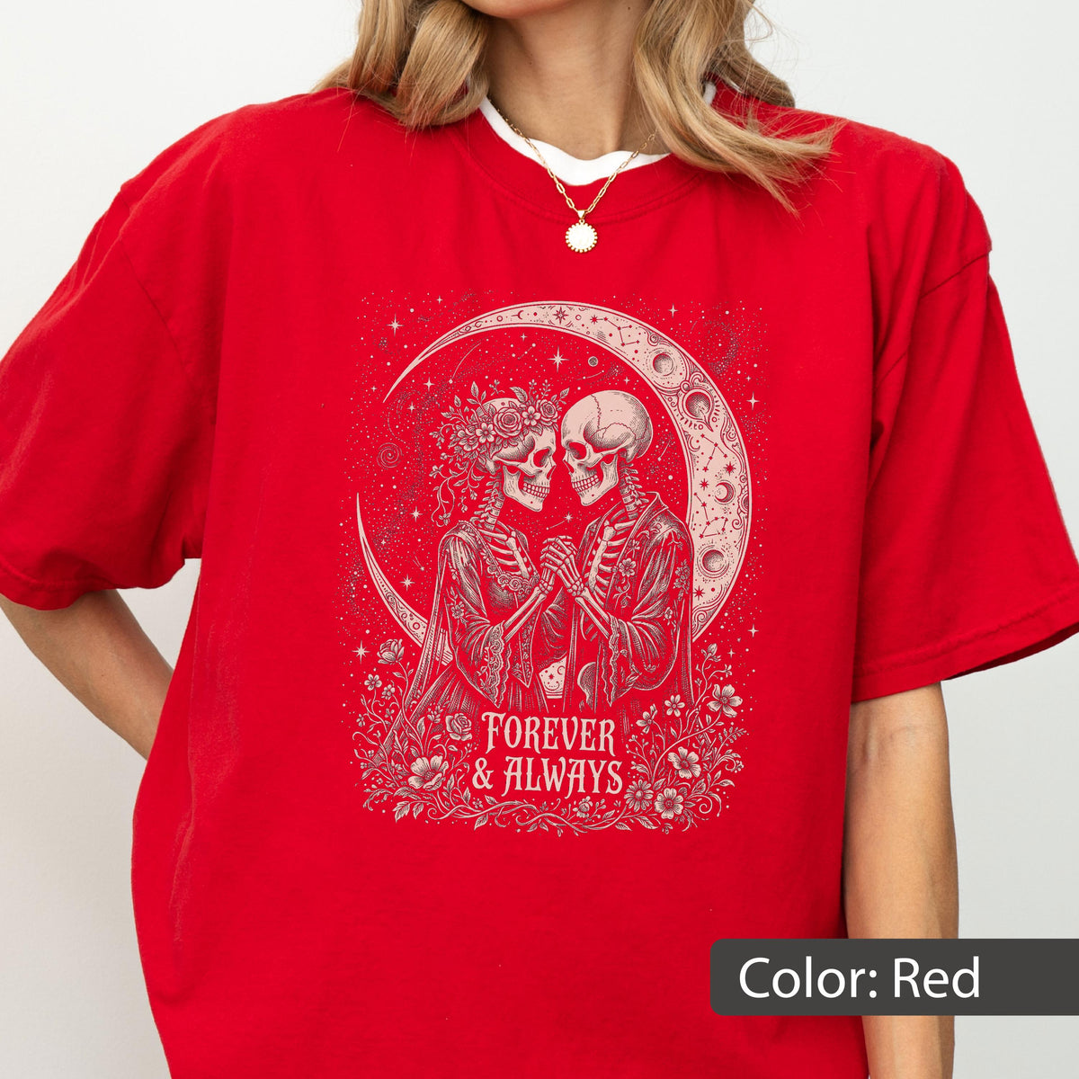May include: A bright red t-shirt featuring a graphic print of two skeletons holding hands under a crescent moon. The design includes floral accents and the text "FOREVER & ALWAYS" in a decorative font. The skeletons are depicted in white ink.