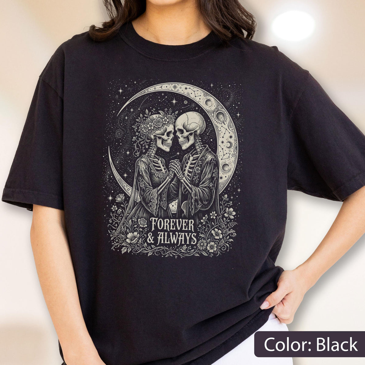May include: A black t-shirt featuring a graphic print of two skeletons holding hands under a crescent moon. The skeletons are surrounded by flowers and stars. Below the illustration, the text reads "FOREVER & ALWAYS" in a decorative font.