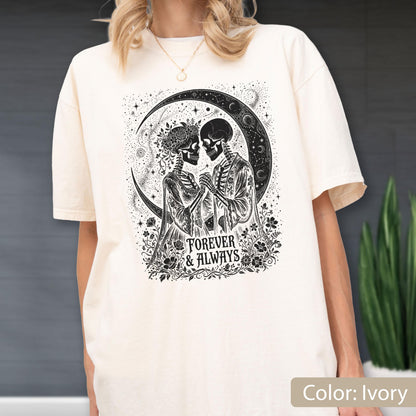 May include: An ivory t-shirt featuring a black graphic print of two skeletons holding hands under a crescent moon. The design includes floral elements and the text "FOREVER & ALWAYS" centered below the figures. The shirt has short sleeves and a crew neckline.