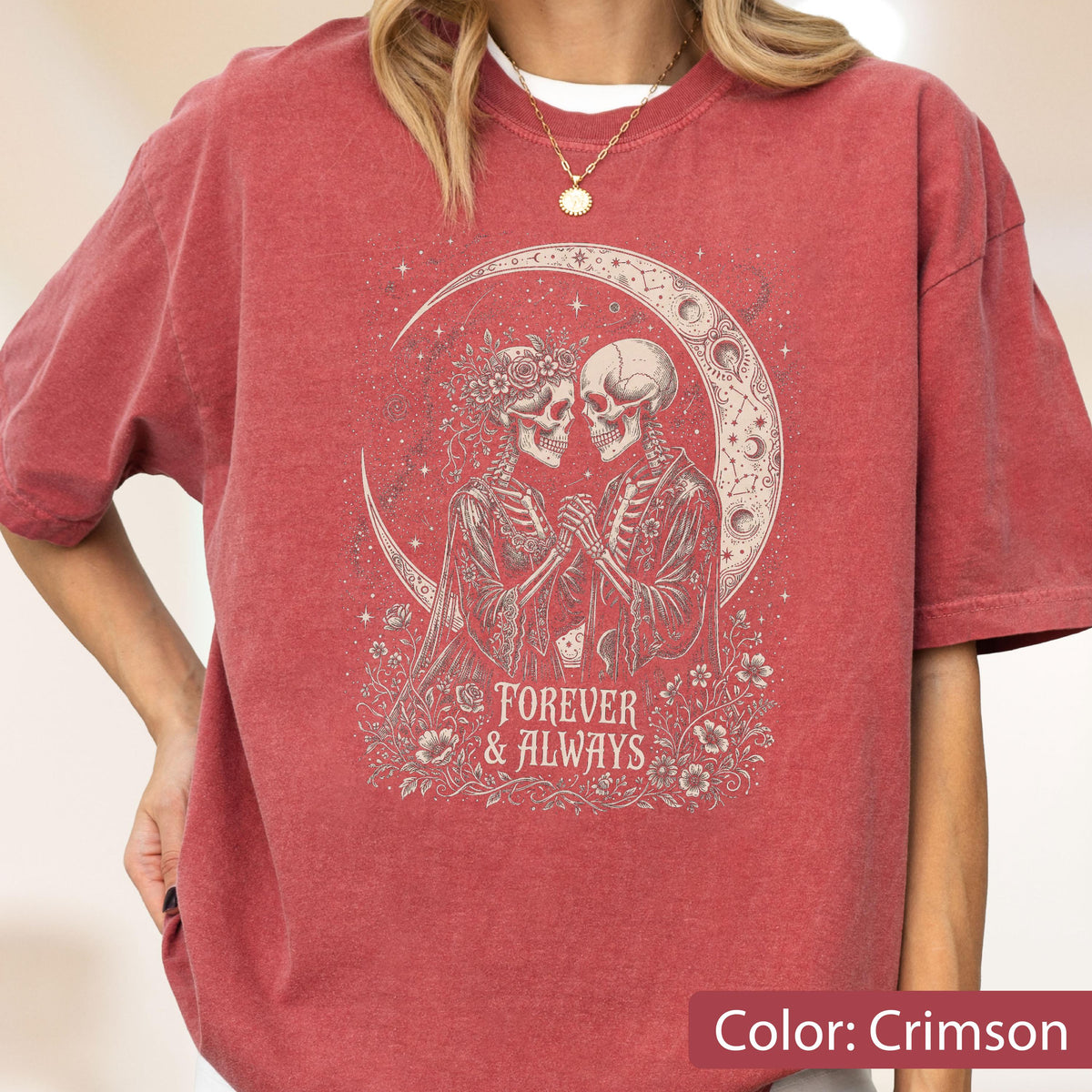 May include: A crimson short-sleeve t-shirt featuring a graphic print of two skeletons holding hands under a crescent moon. The design includes floral accents and the text "FOREVER & ALWAYS" in a decorative font. The shirt has a crew neckline.