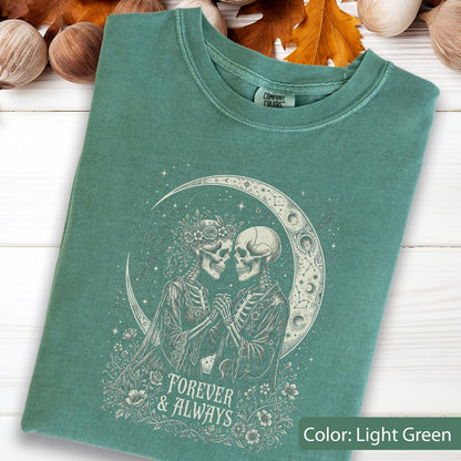 May include: A light green t-shirt featuring a graphic print of two skeletons holding hands in front of a crescent moon. The design includes floral accents and the text "FOREVER & ALWAYS" in a decorative font. The shirt has a Comfort Colors brand label.