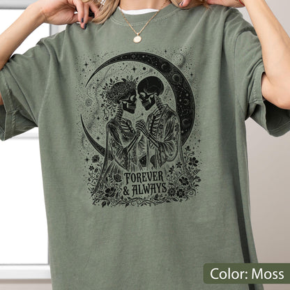 May include: A moss green t-shirt featuring a black graphic print of two skeletons holding hands in front of a large crescent moon. The design includes floral accents and the text "FOREVER & ALWAYS" centered below the skeletons.