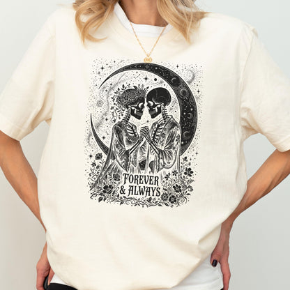 May include: A cream-colored short-sleeve t-shirt featuring a black graphic print of two skeletons holding hands in front of a crescent moon. The design includes floral accents and the text "FOREVER & ALWAYS" printed in a decorative font below them.