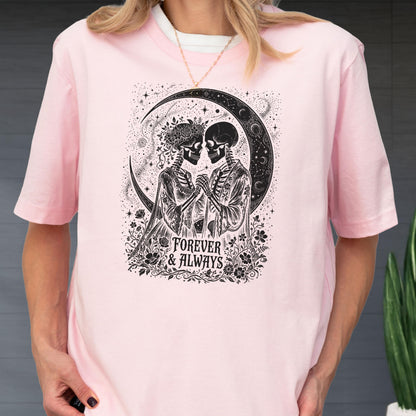 May include: A light pink short-sleeve t-shirt featuring a black graphic print of two skeletons holding hands under a crescent moon. The design includes floral accents and the text "FOREVER & ALWAYS" centered at the bottom of the illustration.
