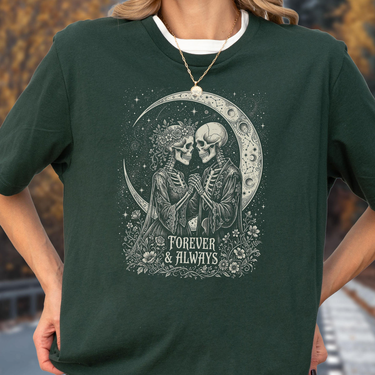 May include: A dark forest green t-shirt featuring a graphic print of two skeletons facing each other, surrounded by flowers and a crescent moon. The text "FOREVER & ALWAYS" is printed below the skeletons in a decorative, serif font style.