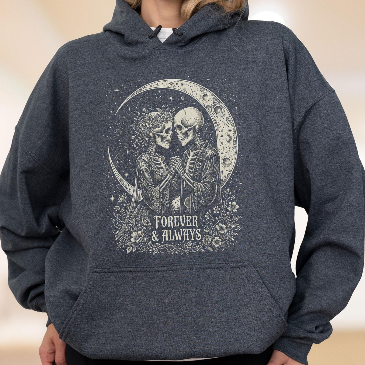 May include: A dark heather gray hooded sweatshirt featuring a graphic print of two skeletons holding hands. The design includes a crescent moon, floral accents, and the text "FOREVER & ALWAYS" centered below the figures in a decorative font.