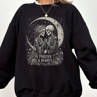 May include: A black long-sleeve sweatshirt featuring a graphic print of two skeletons holding hands under a crescent moon. The skeletons are surrounded by flowers and stars. The text "FOREVER & ALWAYS" is printed in white at the bottom.