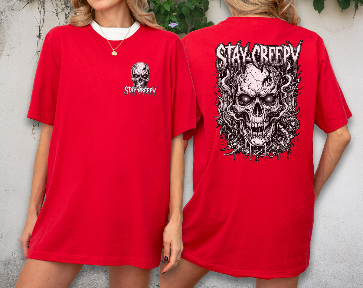 May include: A bright red short-sleeve t-shirt featuring a small graphic of a skull and the text "STAY CREEPY" on the front left chest, and a large, detailed black and white illustration of a skull with swirling smoke on the back.
