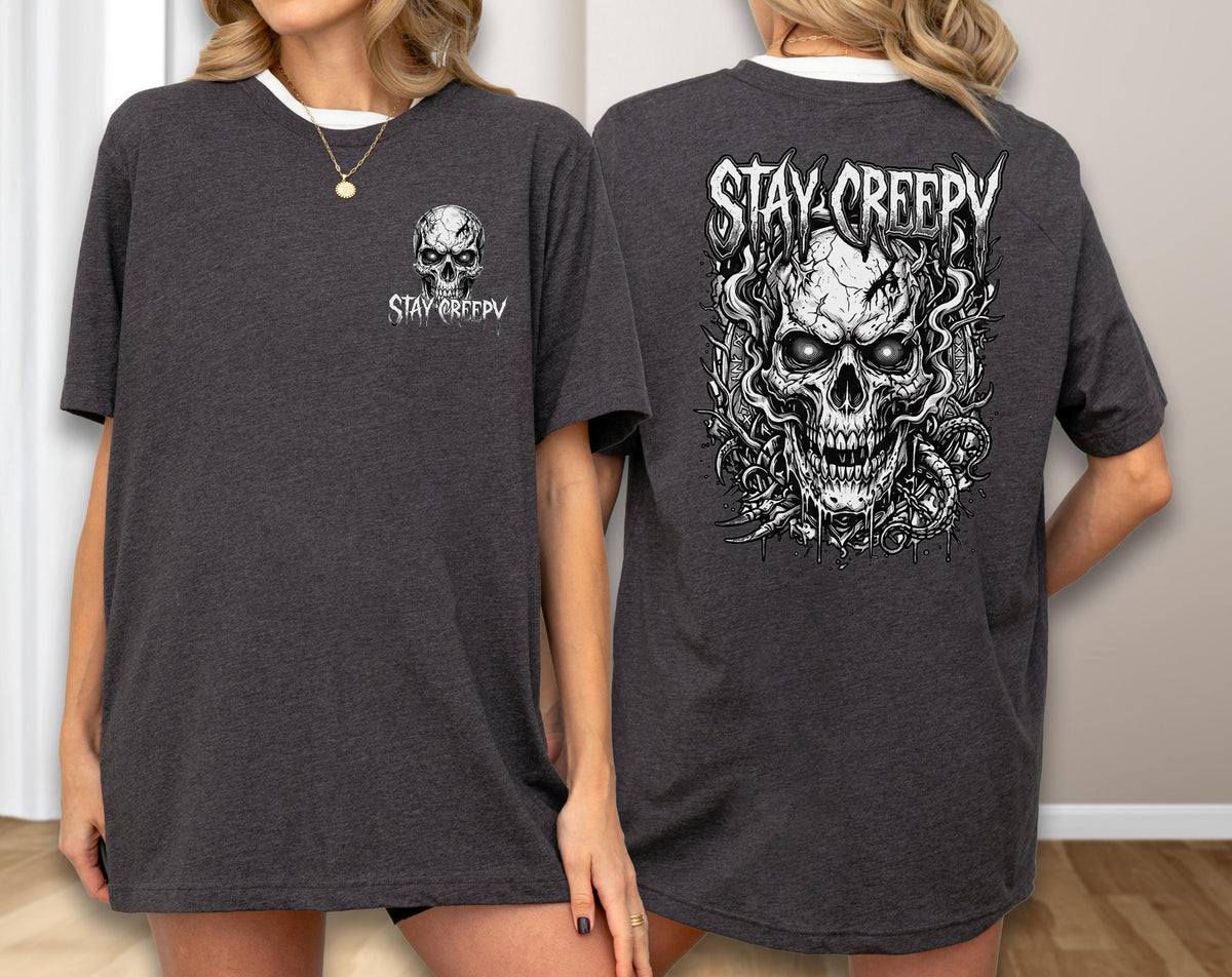 May include: A charcoal gray t-shirt featuring a small white skull graphic and the text STAY CREEPY on the front left chest, and a large, detailed white skull illustration with the text STAY CREEPY printed across the back.