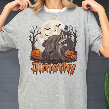 May include: A heather gray t-shirt featuring a graphic of a raccoon walking in front of a full moon, a haunted house, bare trees, and three jack-o'-lanterns. The text "Jimothy" is printed below the illustration in a dripping orange font.