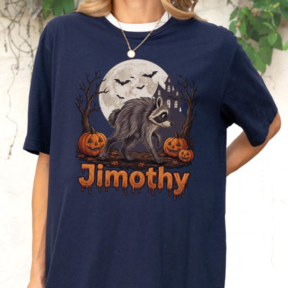 May include: A navy blue t-shirt featuring a graphic of a raccoon standing in front of a full moon, bare trees, and three jack-o'-lanterns. Bats fly in the sky, and the name Jimothy is printed in orange, dripping-style lettering below the scene.