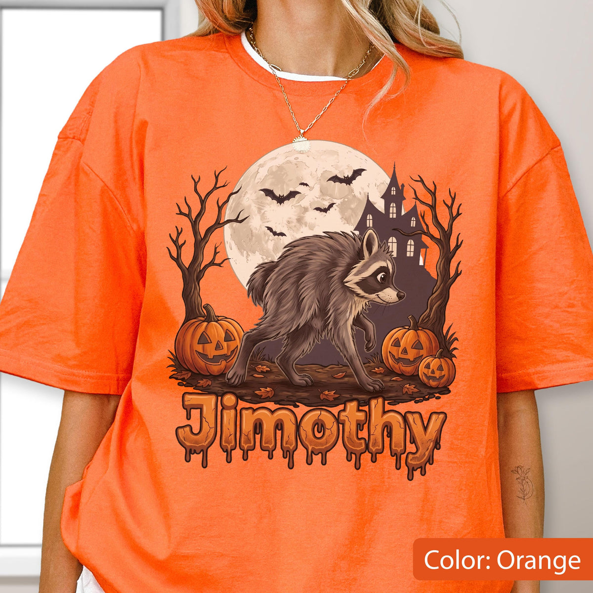 May include: An orange t-shirt featuring a graphic of a raccoon standing in front of a full moon, a haunted house, bare trees, and three jack-o'-lanterns. The word "Jimothy" is printed in a stylized, dripping orange font at the bottom of the design.