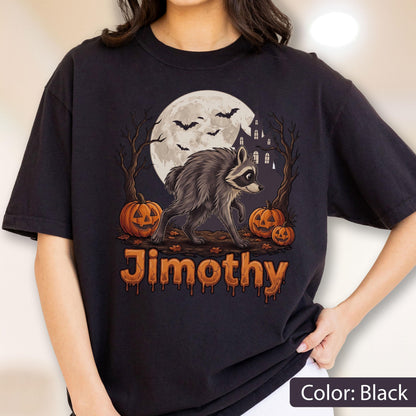May include: A black t-shirt featuring a graphic of a raccoon walking in front of a full moon, bare trees, and a haunted house. Three orange jack-o'-lanterns sit on the ground with bats flying above. The name Jimothy is printed in orange text.