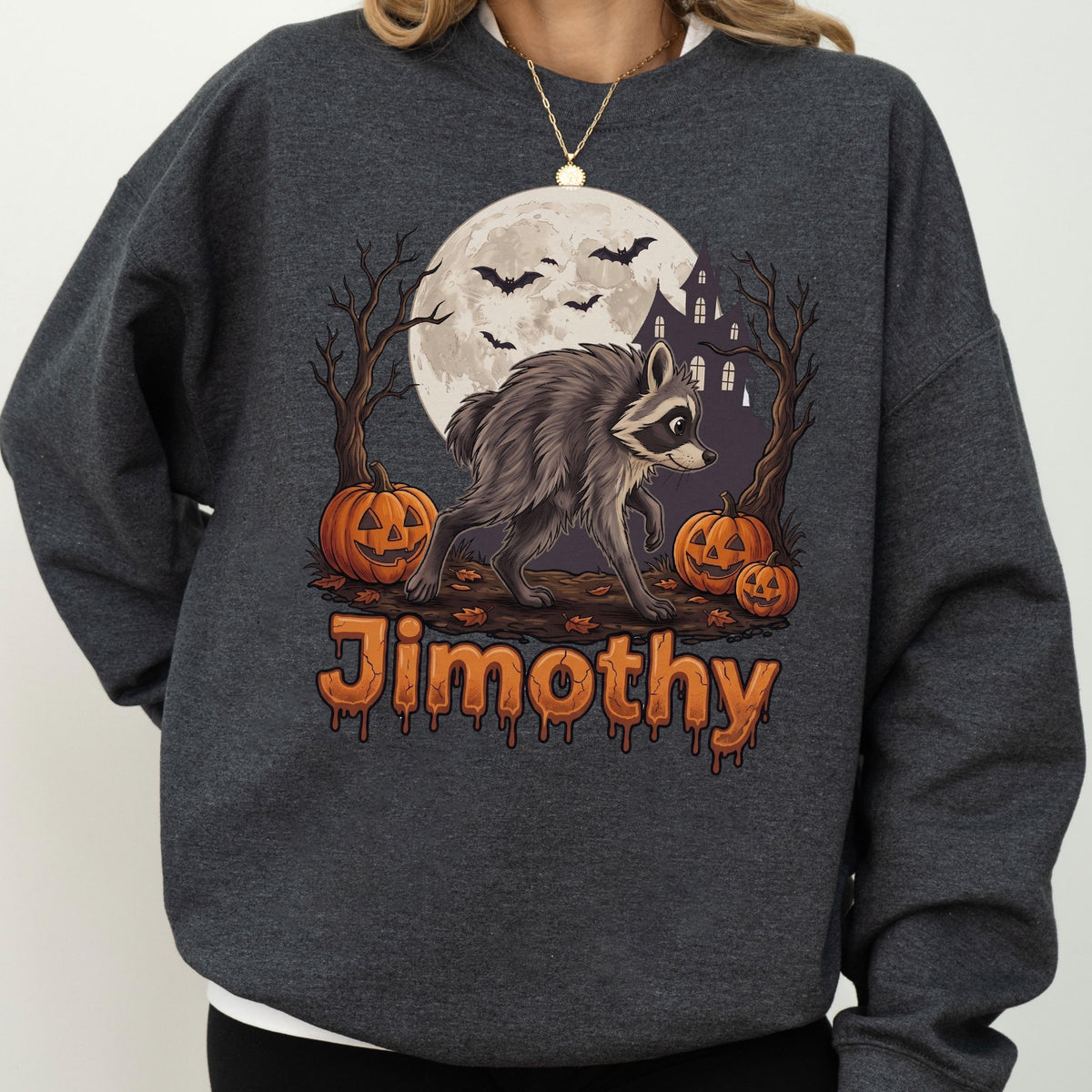 May include: A dark charcoal gray crewneck sweatshirt featuring a graphic print of a raccoon walking in front of a full moon, a haunted house, bare trees, and three jack-o'-lanterns. The name Jimothy is printed in orange below the illustration.
