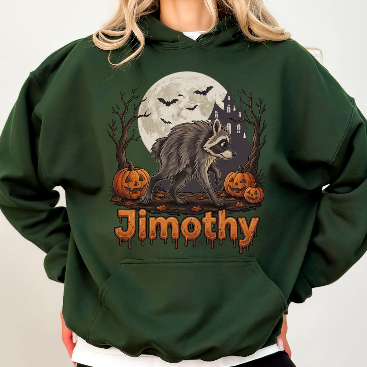 May include: A dark green hooded sweatshirt featuring a graphic of a raccoon standing in front of a full moon, a haunted house, and two jack-o'-lanterns. The text "Jimothy" is printed in orange, dripping-style lettering below the illustration.