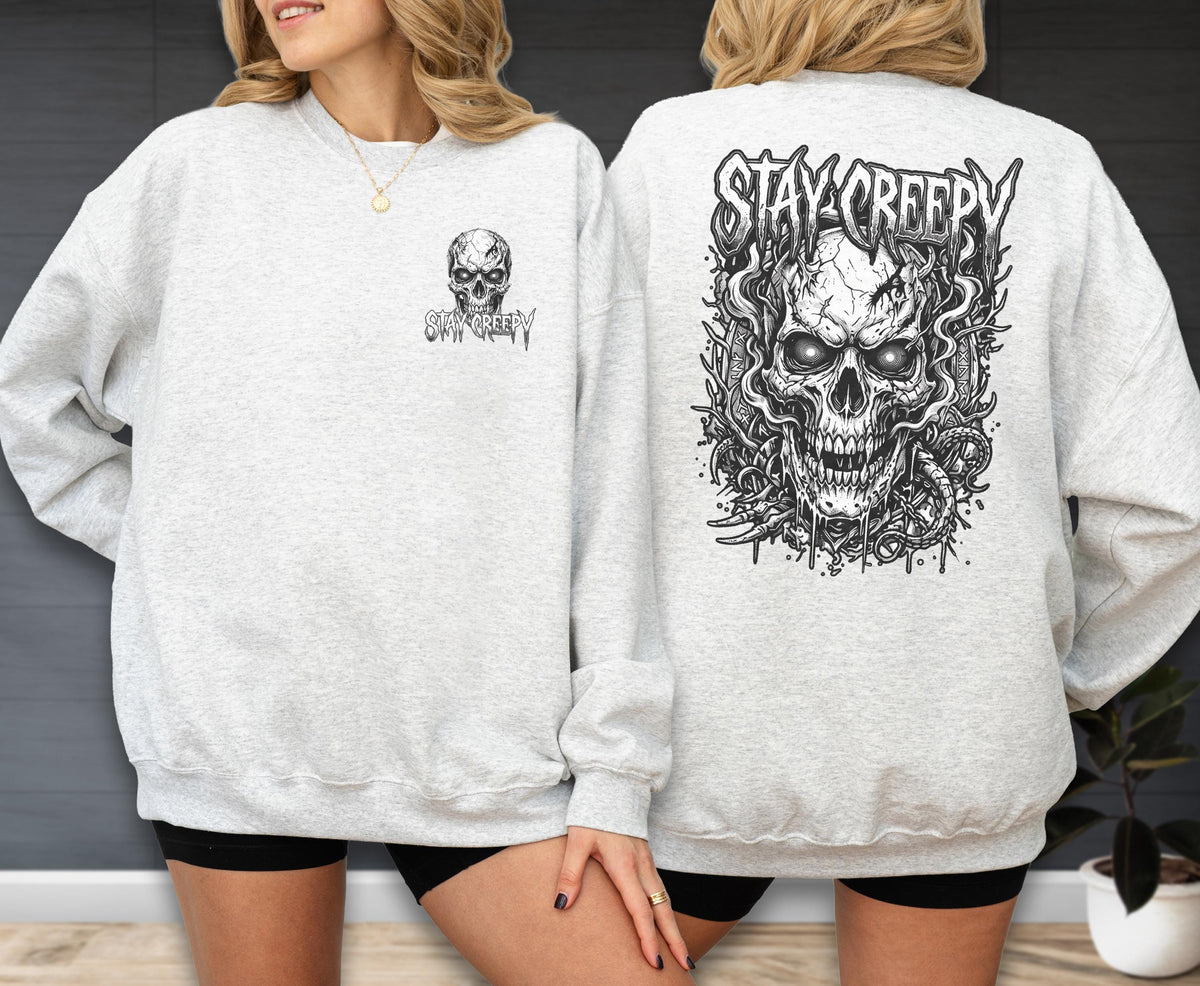 May include: A light gray crewneck sweatshirt featuring a small black skull graphic on the left chest and a large, detailed black skull illustration on the back, both accompanied by the text STAY CREEPY in a stylized, jagged font.