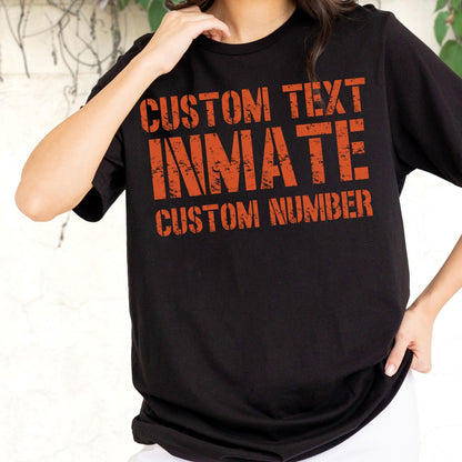 May include: A black short-sleeved t-shirt featuring orange distressed-style text on the front. The text reads CUSTOM TEXT, INMATE, and CUSTOM NUMBER in a bold, blocky font. The design is centered on the chest area of the garment.