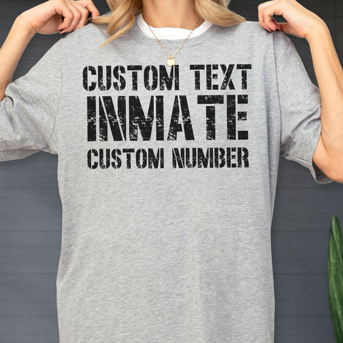 May include: A heather gray short-sleeve t-shirt featuring black distressed-style text printed on the chest. The text reads CUSTOM TEXT, INMATE, and CUSTOM NUMBER in a bold, block-style font. The shirt has a crew neckline and a standard fit.