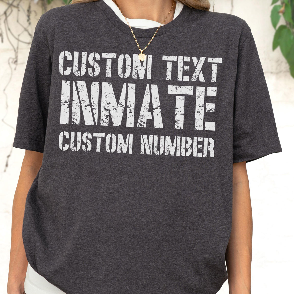 May include: A dark charcoal grey short-sleeved t-shirt featuring white distressed-style block lettering. The text on the front reads CUSTOM TEXT, INMATE, and CUSTOM NUMBER in a stacked layout. The shirt has a crew neckline and a heathered fabric texture.