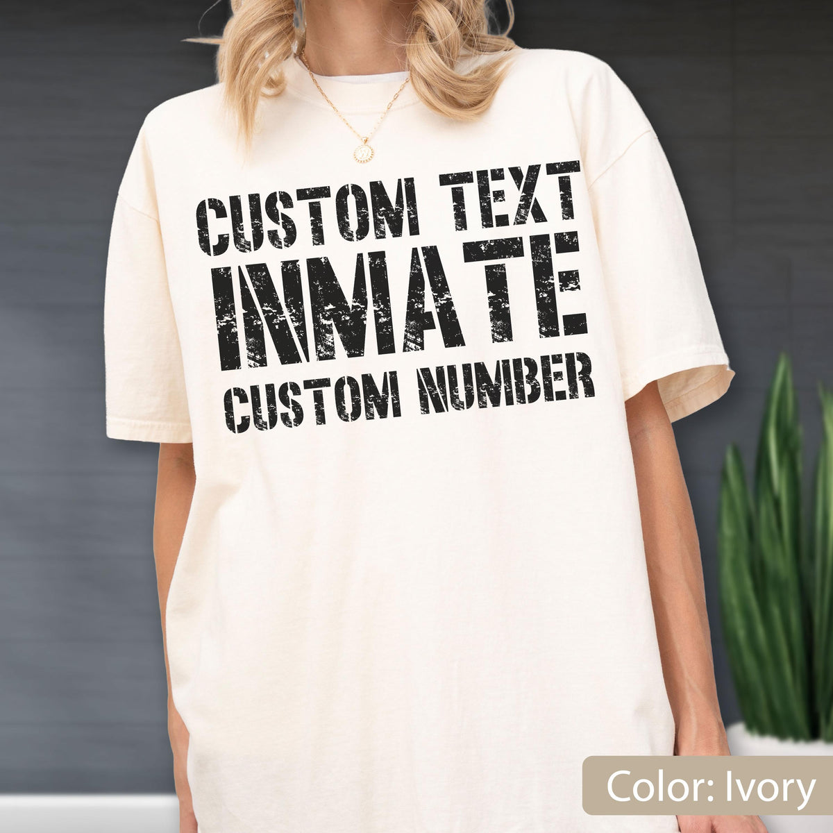 May include: An ivory short-sleeve t-shirt featuring black distressed-style text printed on the chest. The text reads CUSTOM TEXT, INMATE, and CUSTOM NUMBER in a bold, block-letter font. The shirt has a crew neckline and a relaxed fit.