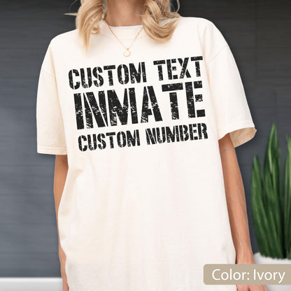 May include: An ivory short-sleeve t-shirt featuring black distressed-style text printed on the chest. The text reads CUSTOM TEXT, INMATE, and CUSTOM NUMBER in a bold, block-letter font. The shirt has a crew neckline and a relaxed fit.