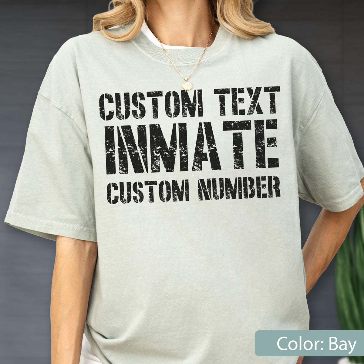 May include: A bay-colored short-sleeve t-shirt featuring black distressed-style text printed on the front. The text reads CUSTOM TEXT, INMATE, and CUSTOM NUMBER in a bold, block-style font. The shirt has a crew neckline and a relaxed fit.