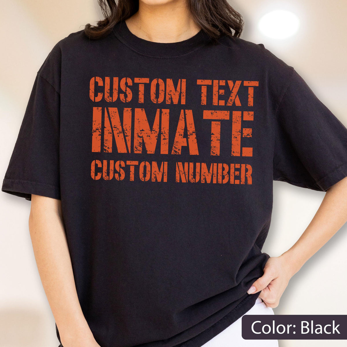 May include: A black short-sleeved t-shirt featuring orange distressed-style text on the front. The text reads CUSTOM TEXT, INMATE, and CUSTOM NUMBER in a bold, blocky font. The design has a weathered, worn appearance across the chest area.