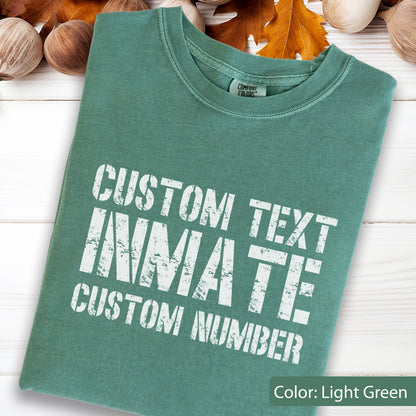 May include: A light green crew neck t-shirt featuring white distressed-style lettering that reads CUSTOM TEXT INMATE CUSTOM NUMBER. The garment has a Comfort Colors brand label visible at the inner neckline and a short-sleeved design.