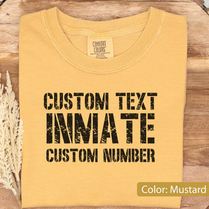 May include: A mustard yellow crew neck t-shirt with black distressed-style text printed on the front. The text reads CUSTOM TEXT, INMATE, and CUSTOM NUMBER. The shirt features a Comfort Colors brand label inside the collar area.