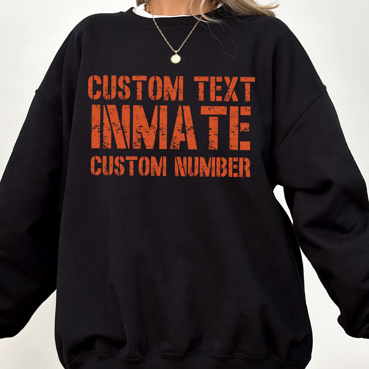 May include: A black long-sleeve crewneck sweatshirt featuring orange distressed-style text on the chest. The graphic reads CUSTOM TEXT, INMATE, and CUSTOM NUMBER in a bold, blocky font. The garment has a simple, solid-colored design.