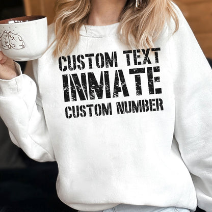 May include: A white crewneck sweatshirt featuring black distressed-style text that reads CUSTOM TEXT, INMATE, and CUSTOM NUMBER. The garment has long sleeves and a ribbed neckline, presented in a clean, simple design for casual wear.