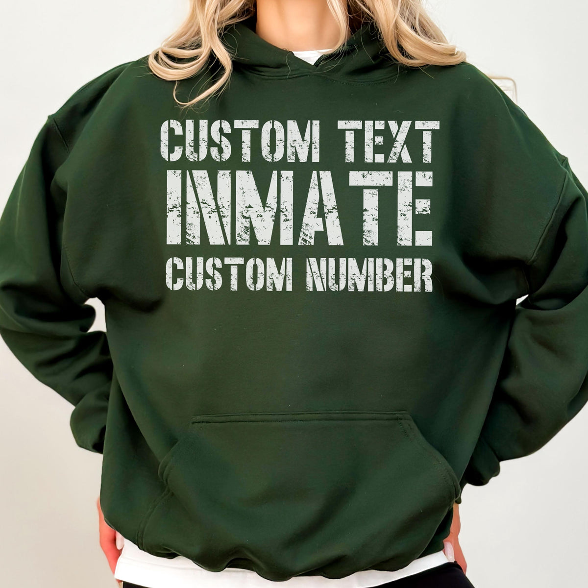 May include: A dark forest green hooded sweatshirt featuring a front kangaroo pocket and white distressed-style lettering that reads CUSTOM TEXT, INMATE, and CUSTOM NUMBER in a bold, block font across the center of the chest area.
