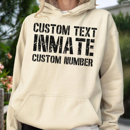May include: A beige hooded sweatshirt featuring black distressed-style text on the front that reads CUSTOM TEXT, INMATE, and CUSTOM NUMBER. The garment includes a front kangaroo pocket, long sleeves, and a drawstring hood with matching beige cords.