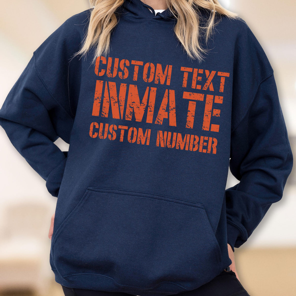 May include: A navy blue hooded sweatshirt featuring a front kangaroo pocket and orange distressed-style text printed on the chest. The text reads CUSTOM TEXT, INMATE, and CUSTOM NUMBER in a bold, blocky font with a weathered, worn-in appearance.