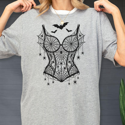 May include: A heather gray t-shirt featuring a black graphic print of a corset made from spiderwebs. The design includes multiple small spiders hanging from the webbed corset and three black bats flying above the neckline of the corset illustration.