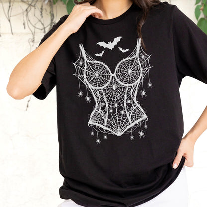 May include: A black short-sleeved t-shirt featuring a white graphic print of a corset design. The corset is composed of intricate spiderwebs and small spiders, with three bats flying above the neckline. The design covers the center chest area.