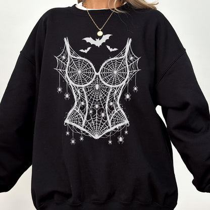 May include: A black long-sleeve sweatshirt featuring a white graphic print of a corset made from spiderwebs. The design includes several small spiders hanging from the webbed corset and three bats flying above the neckline of the corset graphic.