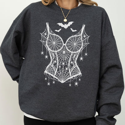 May include: A dark charcoal gray crewneck sweatshirt featuring a white graphic print of a corset made of spiderwebs. The design includes several small spiders hanging from the webbed corset and three bats flying above the bodice area.
