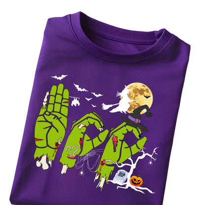 May include: A purple t-shirt featuring a graphic of three green zombie hands forming the word BOO. The design includes a witch on a broomstick, a full moon, bats, a spider web, a tombstone with RIP text, a jack-o'-lantern, and a bare tree.