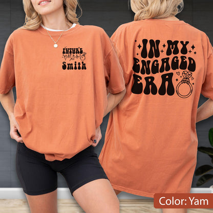 May include: A yam-colored t-shirt featuring black text and graphics. The front displays the text Future Mrs. Smith with a ring icon. The back features the text IN MY ENGAGED ERA in a bold, wavy font, accompanied by small star and heart icons.